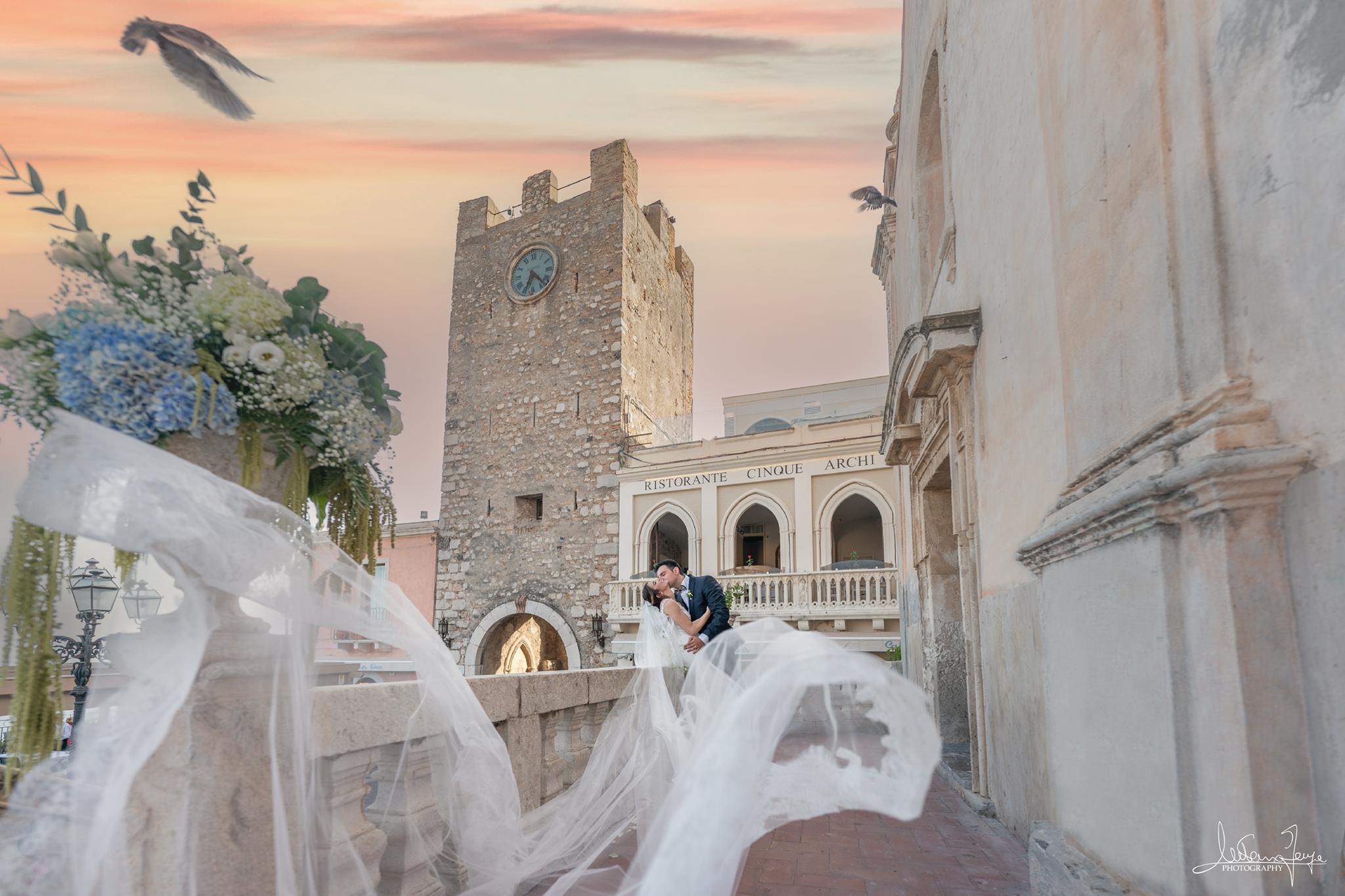 Sposi si baciano a Taormina con il velo della sposa e la Torre dell’Orologio sullo sfondo