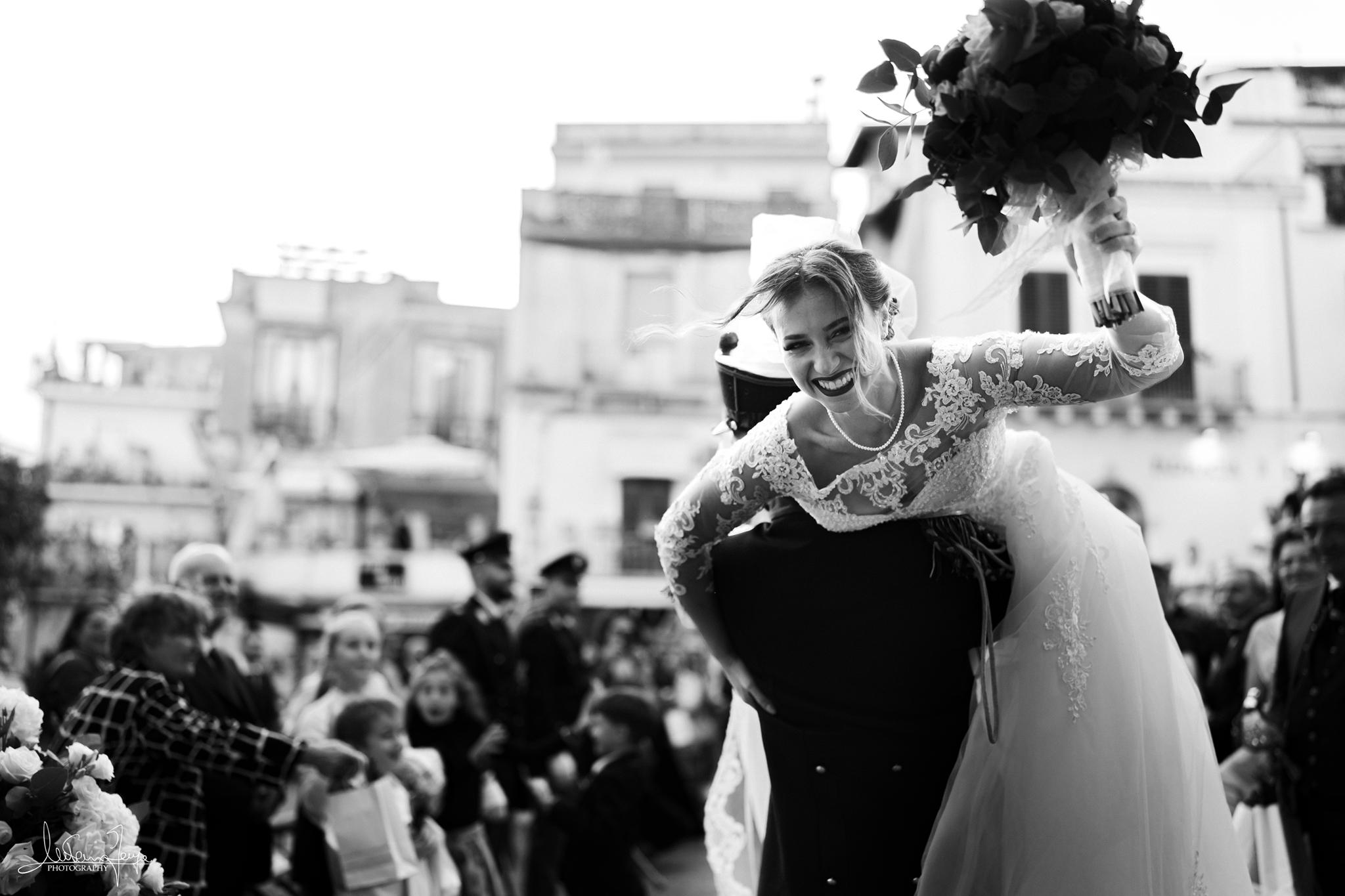 Sposa sorridente in braccio allo sposo con il bouquet alzato